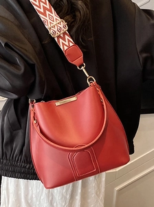 Minimalist red bucket bag with wide geometric strap and golden metal bar accents