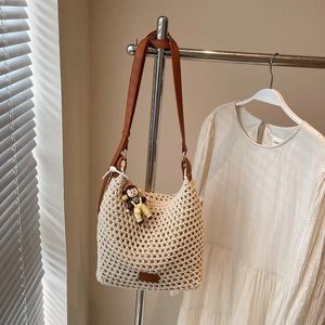 Detail of crochet bucket bag with hollow mesh pattern and small doll charm on brown strap