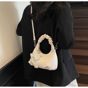 Detail of white half-moon bag with lychee texture leather and a pearl heart pendant