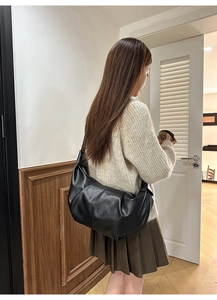 Detailed view of black pleated crescent moon bag with wide shoulder strap on model