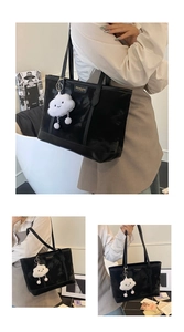 Detail shot of black leather tote bag with Meiduola metal logo and white cloud plush charm