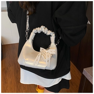 Détail du sac coquillage argenté avec nœud en dentelle, cœur en perles et poignée plissée