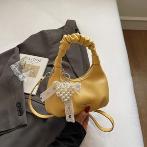 Detail of yellow pebbled leather handbag with ruched handle and pearl heart charm