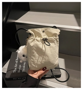 Detail of a creamy white nylon drawstring crossbody bag with a cute plush charm