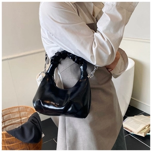 Détail du sac à main brillant avec logo doré, poignée froncée chic et bandoulière