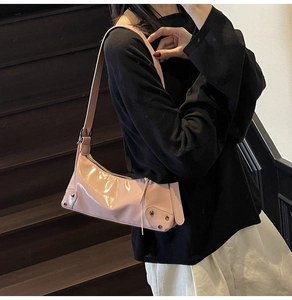 Schultertasche aus rosa Lackleder mit Nieten-Details auf dunklem Holz-Hintergrund