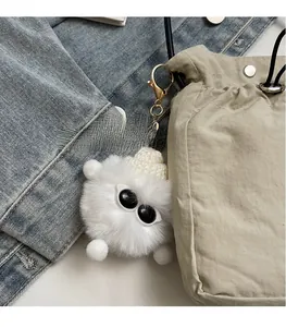 Close-up of white plush ball charm with knit hat on beige drawstring shoulder bag