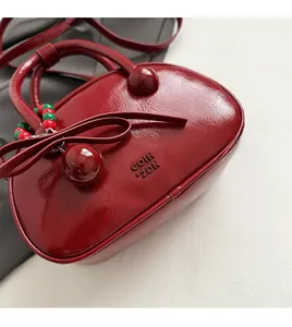 Close-up of wine red pleated bowling bag with beaded charms and leather bow detail