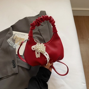 Close-up of red leather crossbody bag with cloud pleated handle and pearl bow pendant