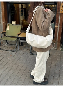 Detailed side view of a white crescent dumpling bag with pleated texture on model