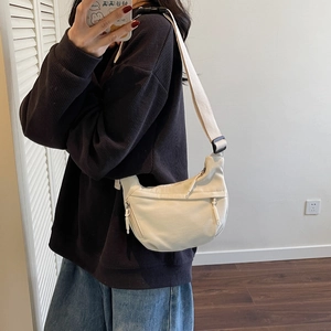 Close-up of cream canvas crescent bag showing wide strap and zipper detail on model