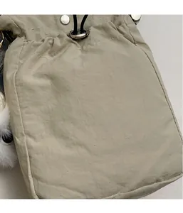 Close-up of beige nylon crossbody bag with drawstring closure and white plush pompom charm