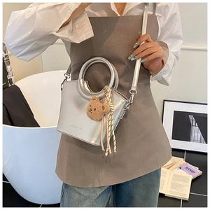 Dettaglio della borsa a mano argento metallizzato con manico tondo e ciondolo orsetto