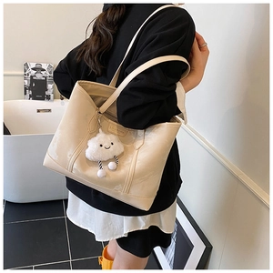 Detail of beige shoulder tote bag with cute plush cloud charm in modern interior