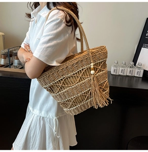 Detail of hand-woven hollow straw tote bag with decorative wooden bead tassels for summer