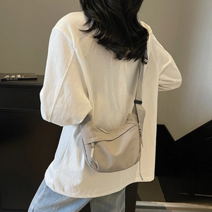 Detail of light grey crescent nylon crossbody bag with adjustable strap and zip pockets
