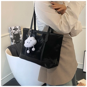 Close-up of black leather tote bag featuring a cute white cloud plush charm and gold logo