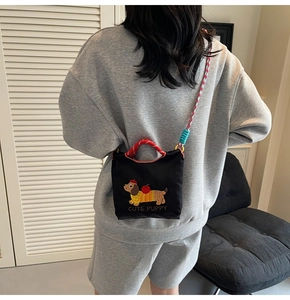 Detail view of cute dachshund embroidery and woven strap on a black crossbody bucket bag