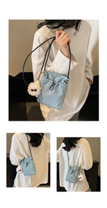 Detail view of light blue canvas bucket bag with drawstring closure and plush charm