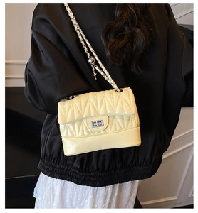 Detail of cream quilted crossbody bag with silver chain strap and metal turn-lock closure