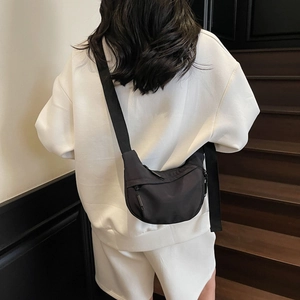 Detailed view of a black nylon crescent crossbody bag worn by a model on white outfit
