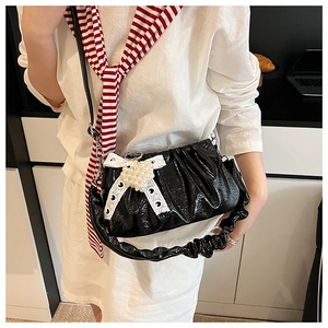 Détail du sac plissé noir brillant orné d'un nœud en dentelle et d'un pendentif perle
