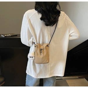 Detail view of khaki mini drawstring crossbody bag with a white plush monster charm