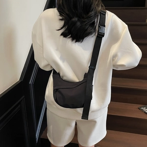 Detail of a black minimalist nylon crossbody bag with heavy-duty buckle on a model