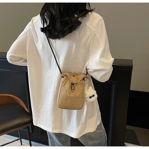 Close-up of minimalist khaki canvas crossbody bag with white plush monster charm on model