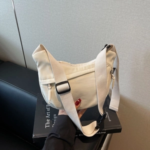 Detail showing the adjustable wide strap and buckle on a cream crescent crossbody bag