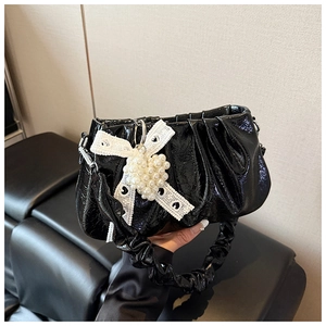 Détail d'un sac plissé en cuir verni noir avec nœud en dentelle et breloque cœur perle