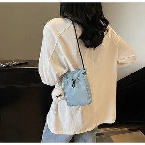Detail of light blue bucket bag with drawstring closure and cute white plush doll charm