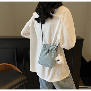 Detail of light blue crossbody bag with drawstring closure and cute white plush charm