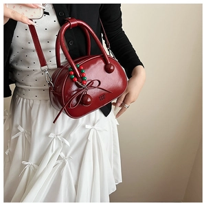 Model showing dark red patent leather bowling bag with bow detail and beaded charm