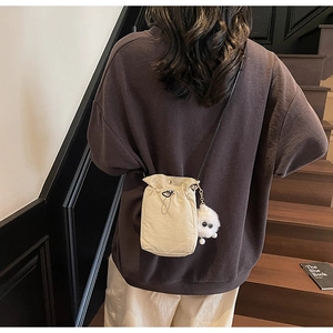 Detail of off-white canvas drawstring crossbody bag with cute monster plush charm