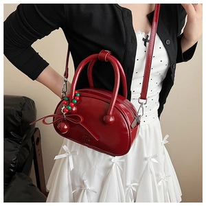 Detail of red patent leather bowling bag with cherry charm and circular top handles