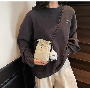 Detail of off-white drawstring crossbody bag with cute monster plush charm on stairs