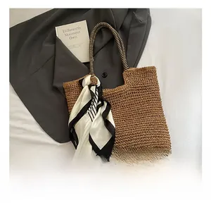 Detail of a woven straw tote bag with black spiral handle and silk scarf on white bed