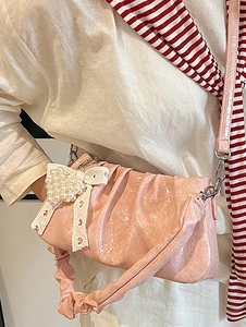Sac bandoulière plissé rose en similicuir avec un nœud orné de perles sur une chemise blanche