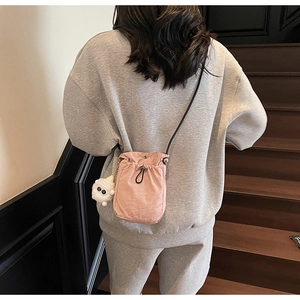 Pink drawstring mini crossbody bag with a cute white plush monster charm on wooden stairs