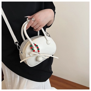 Detail view of white glossy bowling bag featuring red and green bead tassel and bow