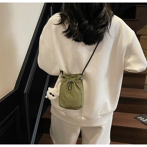 Detail of olive green nylon drawstring bucket bag with cute white plush doll accessory