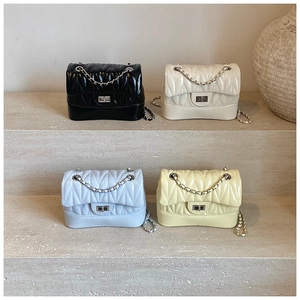 Detail showing four quilted faux leather crossbody bags with metal chains on stone steps