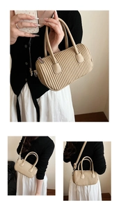 Detail of beige pleated cylinder bag showing dual handles and adjustable shoulder strap