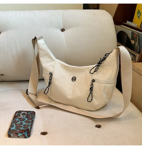 Detail of a creamy white crescent crossbody bag with multi-zipper pockets and metal logo