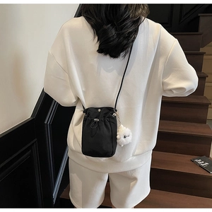 Detail of black drawstring crossbody bag with cute white plush charm on a thin shoulder strap