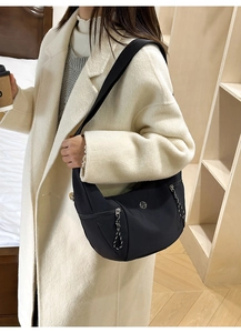 Detail of black nylon crescent bag featuring silver zipper and circular metal logo