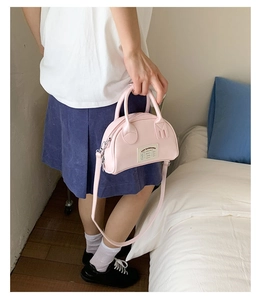 Vue détaillée du sac bowling rose clair avec étiquette blanche et longue bandoulière