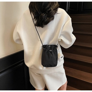 Detail of black nylon drawstring crossbody bag with cute white plush monster charm