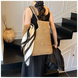 Detail of large straw tote bag with woven texture and decorative striped silk scarf